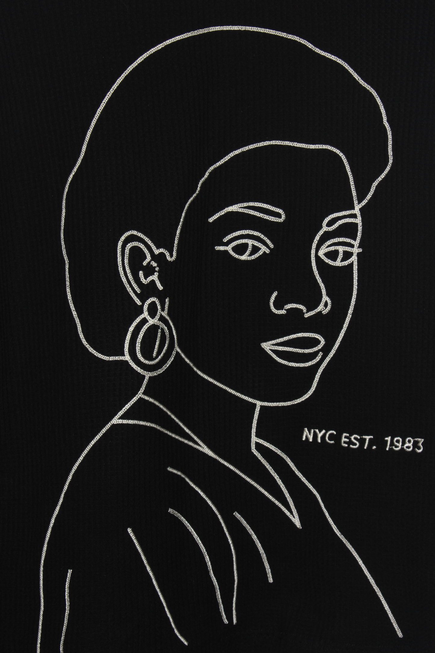 Detail of the La Cara embroidered long sleeve shirt showing cream chain-stitch artwork on a black thermal long sleeve