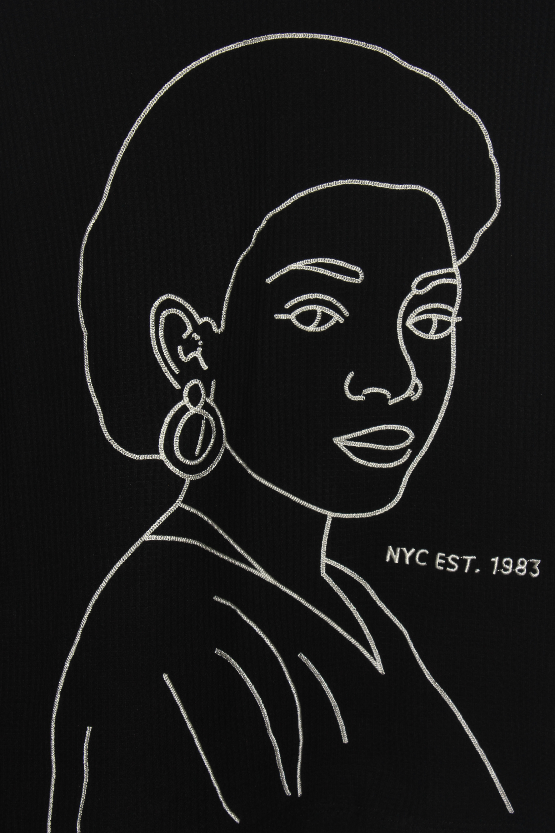 Detail of the La Cara embroidered long sleeve shirt showing cream chain-stitch artwork on a black thermal long sleeve