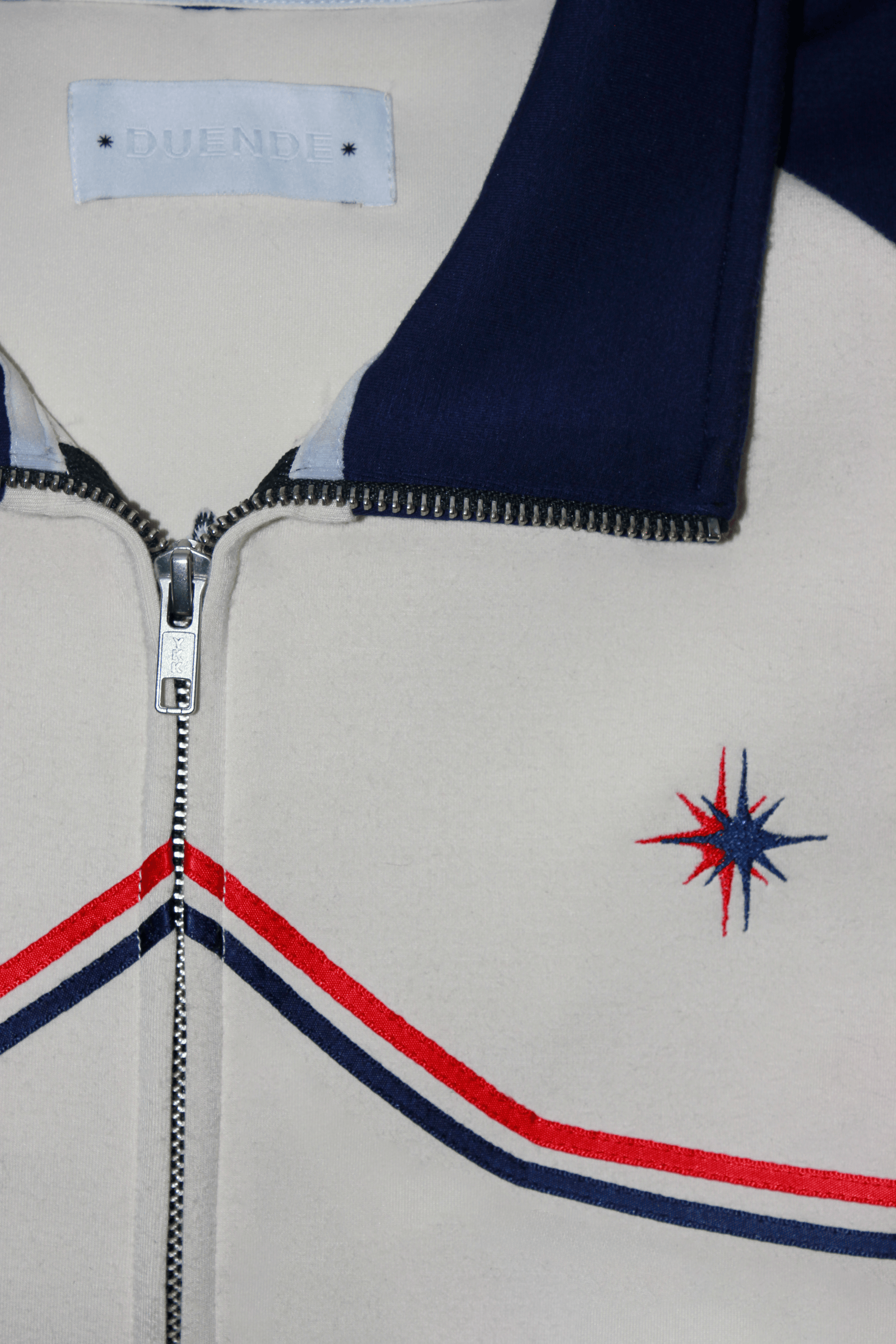 Vidrieras Track Jacket Close Up – premium track jacket and tracksuit jacket style design featuring navy sleeves, cream body, and embroidered DUENDE detailing, perfect as a modern jacket track silhouette